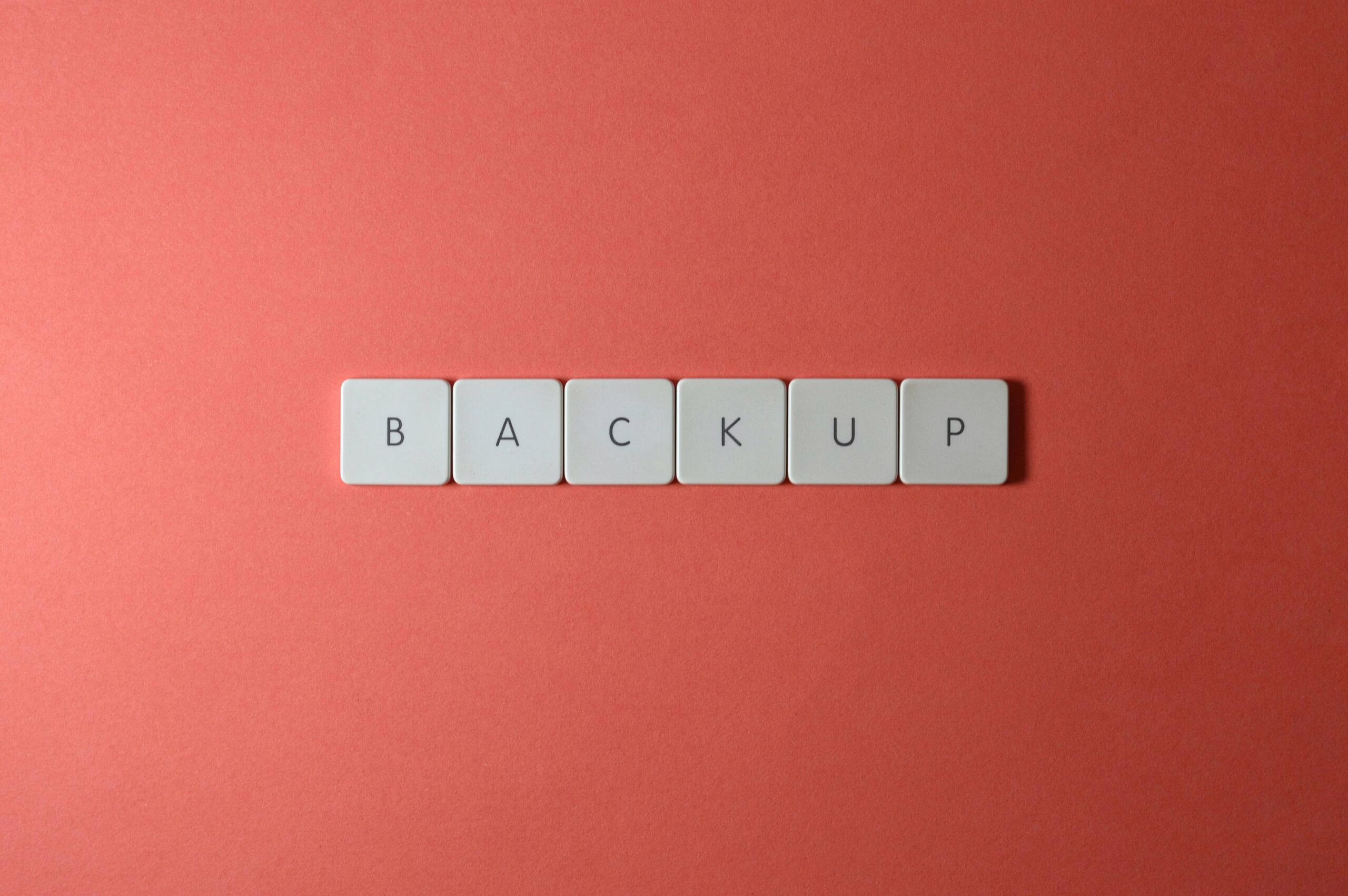 Free Close-up of keyboard keys spelling 'BACKUP' placed on a coral-colored surface. Stock Photo